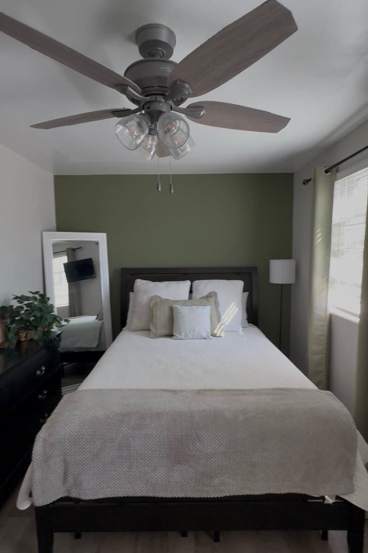 A neatly made bedroom with an olive green accent wall in the Caito home